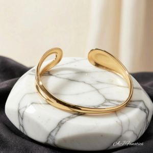 Curve of Contrast Stainless Steel Gold Bangle Bracelet, displayed on a white marble hexagonal stone with a fluid, modern silhouette.