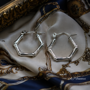 Forest Whisper Minimalist Hoop Earrings in silver‑hued stainless steel with bamboo-inspired hexagon shape, displayed on patterned silk fabric beside an ornate gold frame.