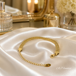 Minimalist Golden Weave Luxe bracelet in polished gold stainless steel with flat woven chain, extender, and lobster clasp displayed on a satin cloth.