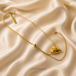 Gold stainless steel necklace with a molten-textured heart pendant and slim adjustable chain, shown on a beige silk background, featuring a diamond‑tipped extender that can be worn at the back or side.