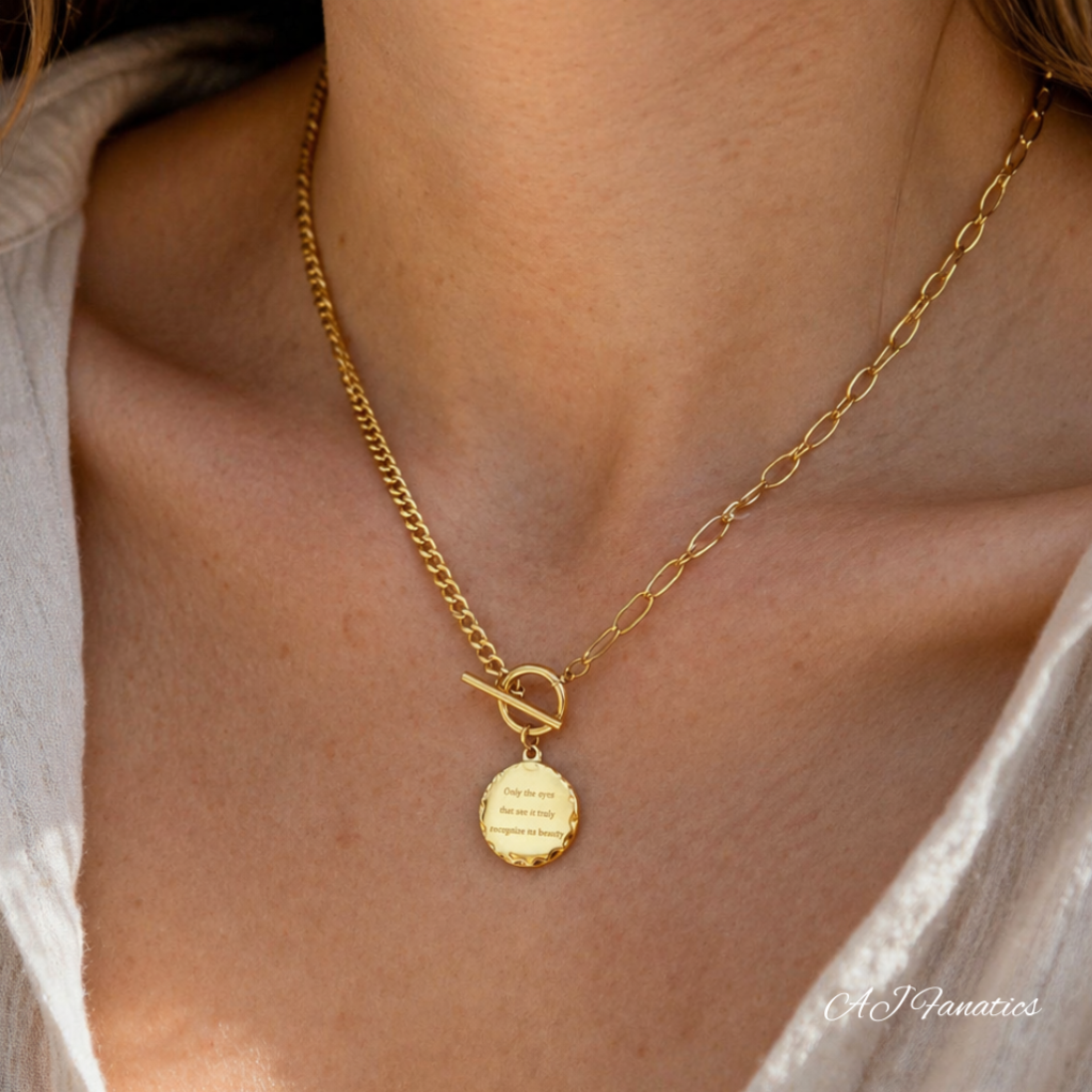 Gold-tone AJ Fanatics necklace with an engraved circular pendant reading “Only the eyes that see it truly recognise its beauty”
